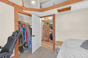 Bedroom with a walk in closet, stacked washer and clothes dryer, light colored carpet, and a closet