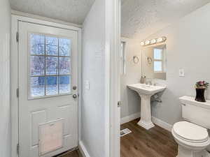 Bathroom with lofted ceiling, wood-type flooring, toilet, and a textured ceiling