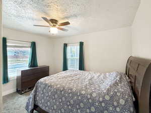 Bedroom with ceiling fan, light colored carpet, and a textured ceiling