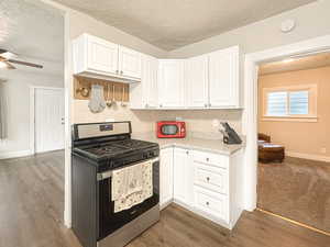 Kitchen featuring white cabinetry, decorative backsplash, stainless steel gas range, and dark hardwood / wood-style floors