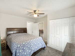 Carpeted bedroom featuring ceiling fan, a closet, and a textured ceiling