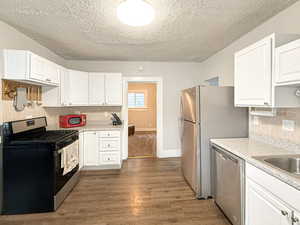 Kitchen with dark wood-type flooring, appliances with stainless steel finishes, backsplash, a textured ceiling, and white cabinets