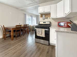 Kitchen with stainless steel gas stove, hardwood / wood-style floors, white cabinetry, a textured ceiling, and decorative backsplash