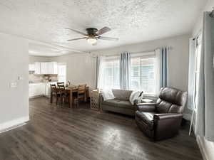 Living room featuring dark wood-type flooring, a textured ceiling, and ceiling fan