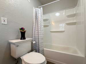 Bathroom featuring toilet and shower / bathtub combination with curtain