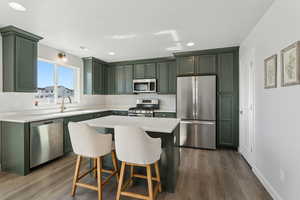 Kitchen with sink, a breakfast bar, stainless steel appliances, dark hardwood / wood-style floors, and a center island