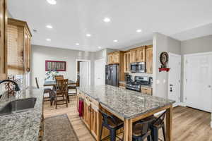 Kitchen with appliances with stainless steel finishes, a breakfast bar, sink, a center island, and light stone counters