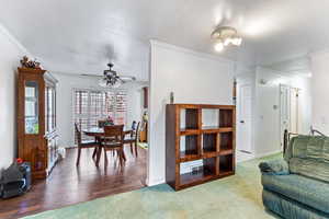 Carpeted living room featuring a textured ceiling, ornamental molding, and ceiling fan