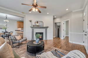 Living room with crown molding, ceiling fan, a fireplace, and hardwood / wood-style floors