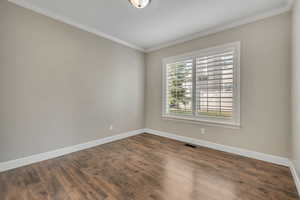 Empty room with dark hardwood / wood-style flooring and crown molding