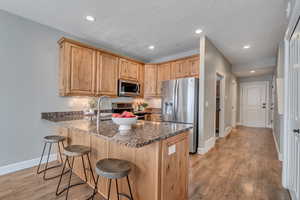 Kitchen with sink, dark stone counters, light hardwood / wood-style floors, kitchen peninsula, and stainless steel appliances