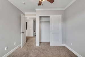 Unfurnished bedroom featuring ornamental molding, light colored carpet, ceiling fan, and a closet