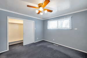 Unfurnished bedroom with crown molding, ceiling fan, and dark colored carpet