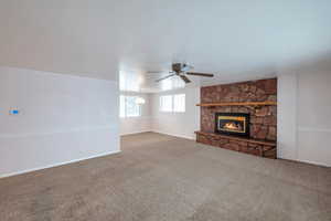 Unfurnished living room with ceiling fan, a stone fireplace, and carpet