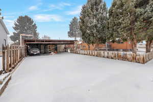 Yard layered in snow featuring a carport