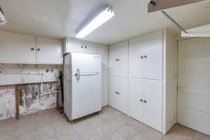 Kitchen with white refrigerator, white cabinetry, and light tile patterned floors