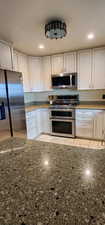 Kitchen with stainless steel appliances, dark stone countertops, and white cabinets