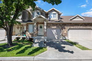Multi unit property featuring stone siding, concrete driveway, a front lawn, and a shingled roof