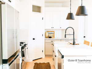 Kitchen with white cabinetry, light stone counters, pendant lighting, stainless steel appliances, and a kitchen island with sink