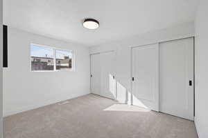 Unfurnished bedroom featuring light carpet, two closets, and a textured ceiling