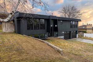 Back house at dusk with a garage and a yard