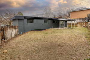 Back house at dusk with a patio and a lawn