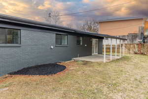 Back house at dusk featuring a patio area and a lawn