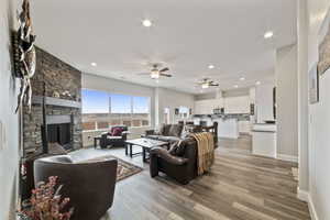 Living room with a stone fireplace, ceiling fan, and light wood-type flooring