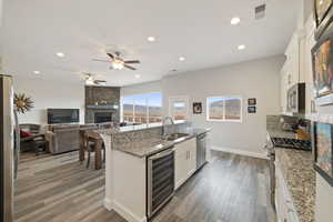 Kitchen with white cabinets, wine cooler, a kitchen island with sink, light stone counters, and stainless steel appliances