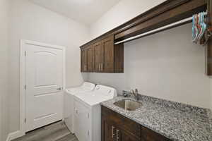 Clothes washing area with sink, hardwood / wood-style flooring, cabinets, and washer and dryer