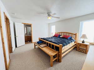 Bedroom featuring ceiling fan, ensuite bath, light colored carpet, and a textured ceiling