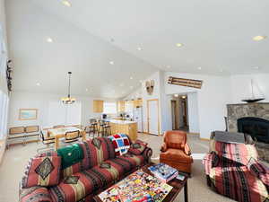 Carpeted living room with a stone fireplace, vaulted ceiling, and a chandelier