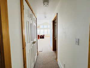 Hallway with vaulted ceiling, carpet floors, and a textured ceiling