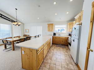 Kitchen with sink, white appliances, light brown cabinetry, decorative light fixtures, and kitchen peninsula