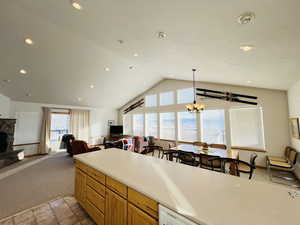 Kitchen with hanging light fixtures, a notable chandelier, a fireplace, vaulted ceiling, and light colored carpet