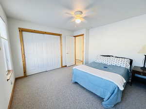 Carpeted bedroom with ceiling fan and a closet
