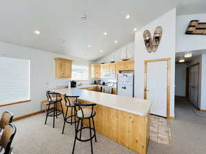Kitchen featuring white appliances, a breakfast bar area, light brown cabinetry, light colored carpet, and kitchen peninsula