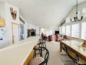 Dining area featuring a stone fireplace, high vaulted ceiling, a chandelier, and carpet