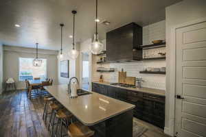 Kitchen featuring a kitchen island with sink, custom exhaust hood, stainless steel gas stovetop, and a kitchen bar