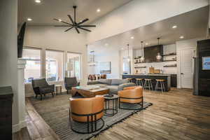 Living room with wood-type flooring, indoor bar, a towering ceiling, and ceiling fan