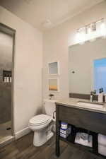 Bathroom featuring hardwood / wood-style flooring, vanity, tiled shower, and toilet