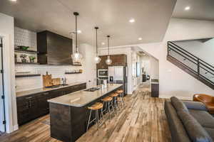 Kitchen with sink, custom exhaust hood, hanging light fixtures, stainless steel appliances, and a center island with sink