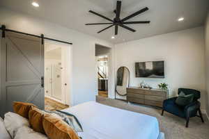 Bedroom with light colored carpet, a barn door, ceiling fan, and ensuite bathroom