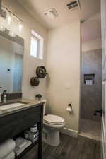 Bathroom with vanity, wood-type flooring, toilet, and tiled shower