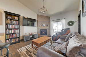 Living room with lofted ceiling, a notable chandelier, a large fireplace, and dark hardwood / wood-style floors