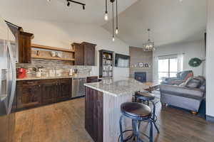 Kitchen with stainless steel appliances, a center island, dark brown cabinetry, light stone countertops, and decorative light fixtures