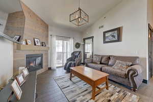 Living room featuring wood-type flooring, a fireplace, high vaulted ceiling, and a notable chandelier