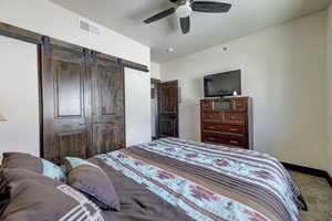 Carpeted bedroom with a barn door and ceiling fan