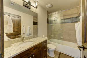 Full bathroom with shower / bath combination with glass door, vanity, toilet, and a textured ceiling