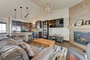 Living room with vaulted ceiling, a fireplace, rail lighting, a notable chandelier, and dark wood-type flooring